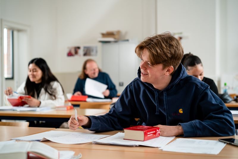 Cursisten zitten aan hun tafel in het leslokaal.